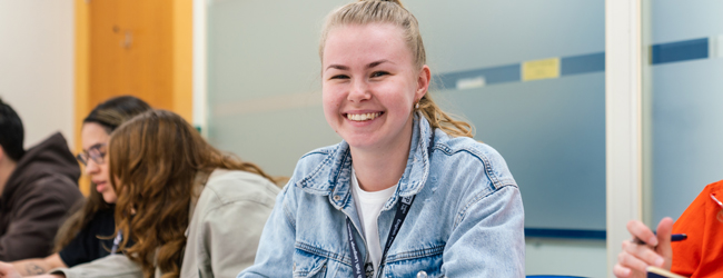 Lächelnde Schülerin sitzt im Klassenzimmer und nimmt am Unterricht während einer LISA! Sprachreise in Leeds teil