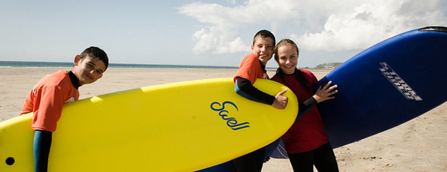Surfkurs bei einer Sprachreise für Schüler in Jersey Drei Schüler tragen Surfbretter am Strand von Jersey