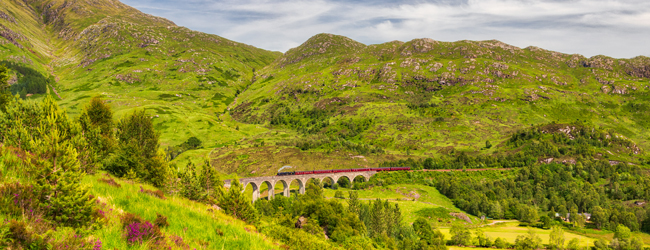 Schottische Landschaft mit Bergen und dem Hogwartsexpress auf einer Steinbrücke