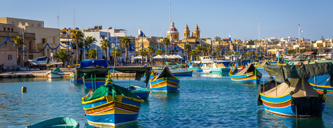 Bunte Fischerboote Malta blaues Wasser mit historischen Kirchen im Hintergrund während einer Schülersprachreise in Sliema