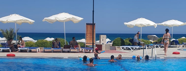 Menschen schwimmen im Pool und liegen auf Sonnenliegen, im Hintergrund das Meer in Nordzypern