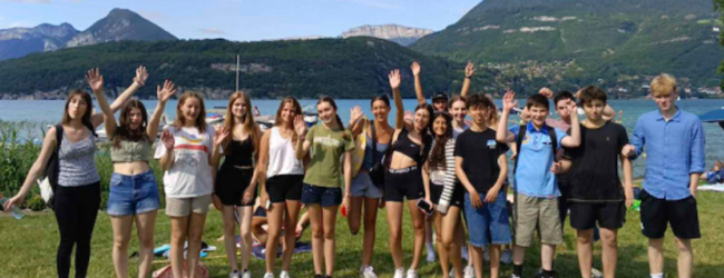 Viele Jugendliche winken in die Kamera vor dem See in Annecy mit Berge im Hintergrund