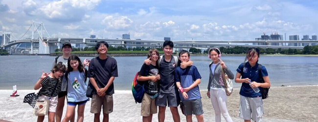 Eine Gruppe Kinder steht vor der Skyline von Tokio am Meer mite iner Brücke im Hintergrund